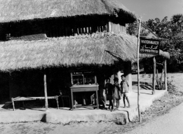 Local kids hang out at a thatched-roofed building advertising "Watch Maker."  Scenes in India witnessed by American GIs during WWII. For many Americans of that era, with their limited experience traveling, the everyday sights and sounds overseas were new, intriguing, and photo worthy.