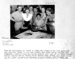 Cooks Ruth Carrell, Betty Yeaton, Jinx Falkenburg visit the enlisted men's mess of the "China Blitzer" fighter squadron and the "Flying Horse" fighter group. The cooks are (left to right): Sgt. Joseph Chirko,  Ruth Carrell, S/Sgt. Steve Nagy, Betty Yeaton, Jinx Falkenburg. In front is "Collen", Burmese refugee and mess attendant, in the background with glasses is Mr. John Woo, Hostel Manager.