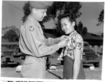 Miss Ulian Hhoo of Singapore receives the Meritorious Civilian Service Award from Col. Richard H. Wise for her work with the American Army in China. Since August 1943 she had worked in the office of a sector surgeon as typist for the medical supply section, laboratory technician, and surgical nurse in the base dispensary operating room.