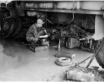 An American GI repairs a transport truck of the 14th Air Force in China, working in rough conditions on flooded ground.