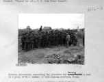 Chinese interpreter explaining the procedure for serving a meal to a group of Miao (ethnic) workers at the Laohwangping (Laohuangping) Airfield, China, in January, 1945. The control tower for the airbase can be see in the distance on the left.