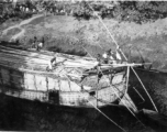 Numerous boatmen use poles to push a large boat in a waterway in India during WWII.