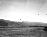 Several P-40 fighters pass over the runway and begin a "break out" to land at Yangkai, Yunnan province. The nose guns of an American B-25H bomber are visible at the far right of this picture taken in the CBI.