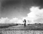 A farmer or laborer in China posing with a should pole. During WWII. Notice the freshly spread stone in the foreground, almost certainly crushed by hand, then hauled to the location by hand (for example, using shoulder poles), then spread and tamped down by human labor.