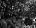 A Chinese officer makes a toast or speech as SACO members share a meal with Nationalist soldiers, in the shade of trees, during WWII. In northern China.