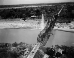 In this image, a bridge somewhere in southwest China, Indochina, or Burma, is bombed by American B-25s, running in very fast at almost tree-top level (notice the perspective of the camera, which is very close to the ground level), with bombs dropping in the river around the bridge. Three to four splash sites can be seen. The bombers come in so fast and unexpectedly that people on the bridge are caught unprepared, as in the blown up image below, where men (either workers or Japanese soldiers) can be seen fra