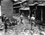 Armed GIs walk on road at Yangkai village, as villagers look up and take note. During WWII.