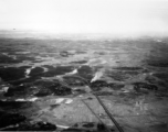 A B-25 flies above a smoking village on a railway in SW China, French Indochina, or Burma, in the CBI, during WWII.