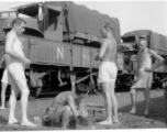 US soldiers bathing at a faucet during war, alongside a railway.