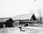 A child stands before a thatch house on stilts in Burma, with a jeep parked nearby.  Near the 797th Engineer Forestry Company.  During WWII.