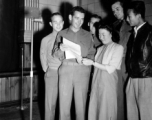 A group of Americans and two Chinese prepare to sing off a sheet of paper into a microphone.