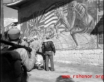 Americans and Chinese stop to look at a large wall mural showing peoples from four countries (China, Britain, United States, Russia, as shown by the four flags) uniting to put fascists in their place.