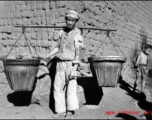 Rural worker with baskets on a shoulder pole. Local people in China, probably in Yunnan province during WWII.