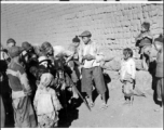 A photographer interacting in a village in Yunnan province.  He's a corporal, so he hasn't been in the service very long. The pith helmet he's wearing is something GIs frequently bought in India on their way into China. The Speed Graphic he's shooting is a late model (earlier Graphics did not did not have the Military ID plate on the bottom of the door).