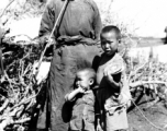 Local rural people in China: An elderly man smokes a long pipe while watching over two children.