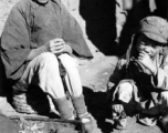 Local people in China: An elderly woman---possibly working as a petty seamstress doing minor repairs on shoes or cloth items---sits with child. During WWII.