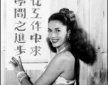 Jinx Falkenburg poses with a classroom slogan that says, roughly, "from cooperation seek progress in learning." In China during WWII.