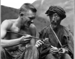 A GI inspects smoking pipe of local man in China, while local man holds western-style pipe. During WWII.  Photo by Syd Greenberg.