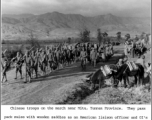 Chinese troops march near Mitu, Yunnan province, during WWII. They pass pack mules with wooden saddles as an American liaison officer and GIs (right center beyond mules) watch the passing parade.  US Signal Corps Photo.