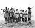 Indian soldiers march being led by a man blowing a horn, with wooden poles substituting for rifles.  Scenes in India witnessed by American GIs during WWII. For many Americans of that era, with their limited experience traveling, the everyday sights and sounds overseas were new, intriguing, and photo worthy.