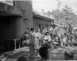 Celebrities (including Ann Sheridan, Ben Blue, and Ruth Dennis on instrument in this shot) perform on an outdoor stage set up at the "Last Resort" at Yangkai, Yunnan province, during WWII. Notice both Americans and Chinese in the audience for this USO event.